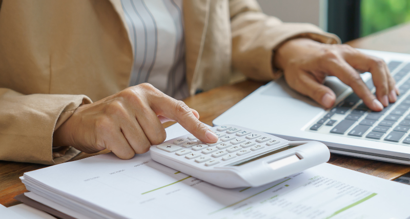 image of person's hands on a calculator and laptop, calculating costs