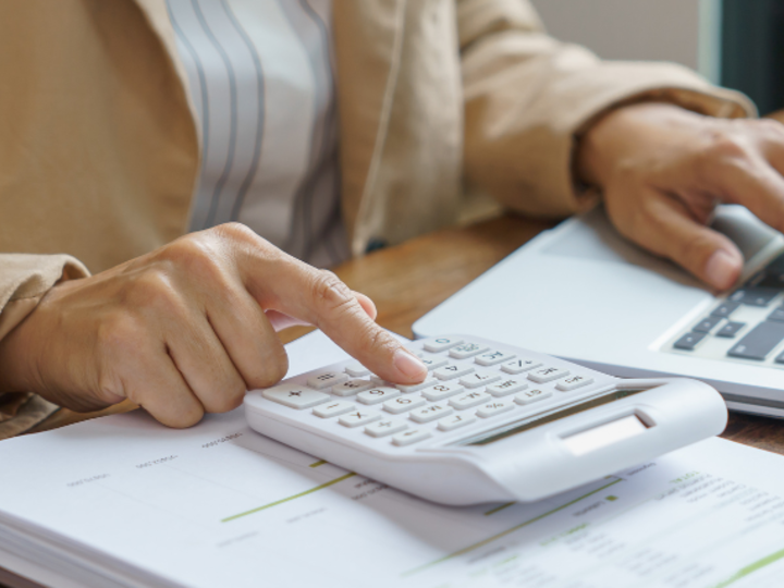 image of person's hands on a calculator and laptop, calculating costs