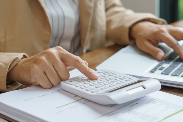 image of person's hands on a calculator and laptop, calculating costs